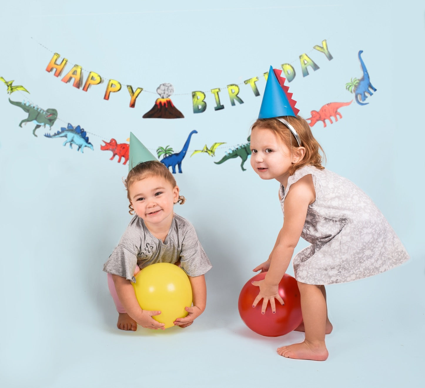 colorful dinosaur birthday banner with two kids in party hats holding balloons dinosaur theme from Parte Haus party supply store in Bethesda MD