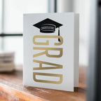 White and gold graduation greeting card with cap design for graduation from Parte Haus party supply store in Bethesda Maryland