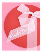 White bride to be bow bridal shower sash on pink and red background from Parte Haus party supply store in Bethesda MD.