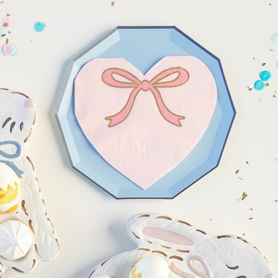 Pink heart napkin with gold bow design for Easter on blue plate from Parte Haus party supply store in Bethesda MD